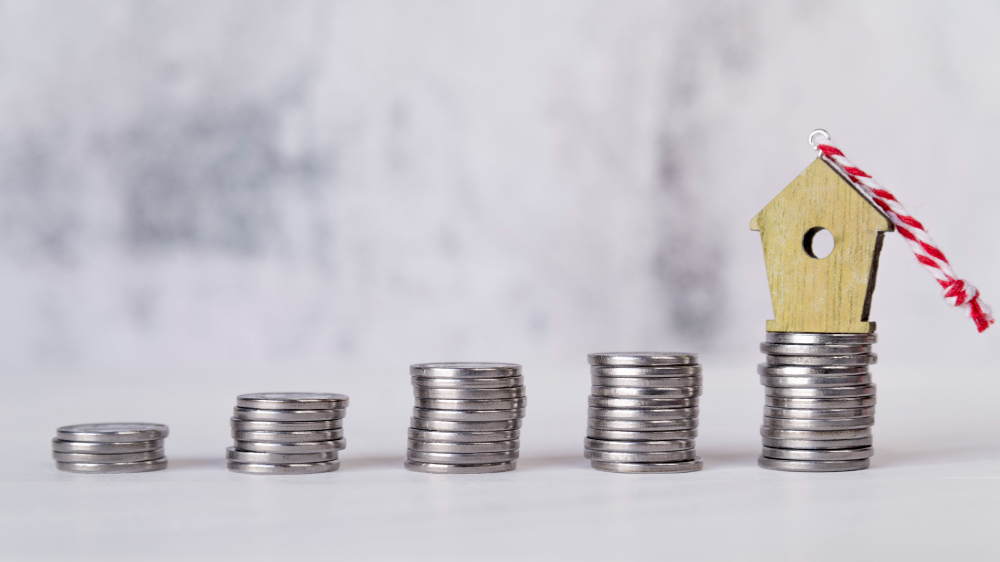 Miniature house put on the biggest of an increasing stacks of silver coins